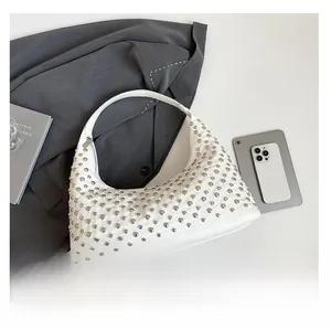 Detail view of white leather hobo bag with silver rivet studs on a grey suit background