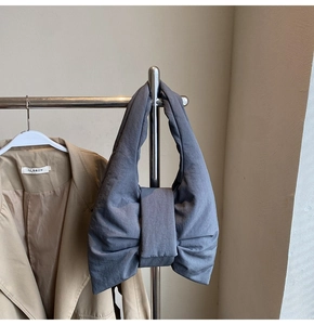 Detail of grey bow-shaped puffy nylon tote bag styled on a rack with a blazer