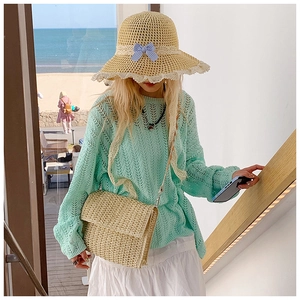 Close-up of mint green knit top paired with straw hat and crossbody bag on beach stairs
