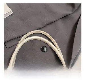Close-up of beige leather handle on tote bag with minimalist grey suit background