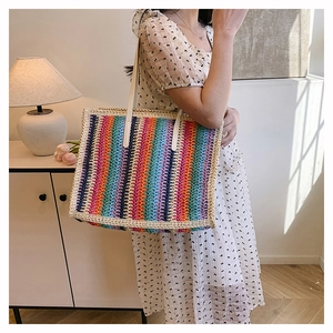 Detail of colorful rainbow woven straw tote bag featuring long cream shoulder straps