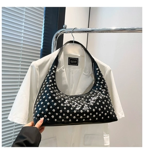 Close-up of black glossy hobo bag with silver studs hanging on a white blazer coat