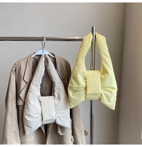 Detail of soft puffy bow shoulder bags in beige and yellow with padded nylon texture