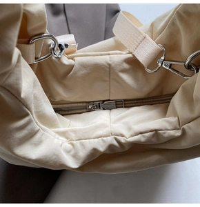 Detail of light beige quilted tote bag showing zipper closure and silver metal hardware