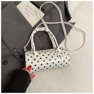 Detailed view of white polka dot cylinder bag on grey suit and white fabric backdrop