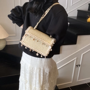 Beige straw woven crossbody bag with seashell fringes and chain strap for beach vacations