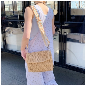 Outdoor shot of a woven straw crossbody bag featuring a geometric embroidered wide strap