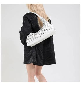 White rivet tote bag worn on shoulder by model over a textured black coat outfit