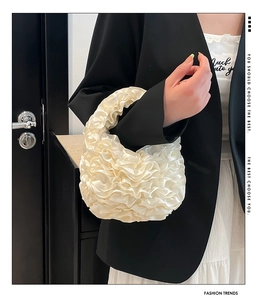Detail of cream white pleated ruffle handbag featuring glossy satin finish texture