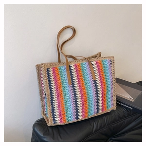 Detail of colorful rainbow striped straw tote bag with brown leather handles on a sofa