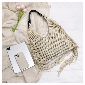 Detail of hand-woven beige mesh tote bag with long tassels and black leather strap