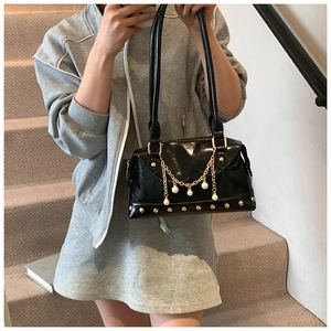 Detail of glossy black patent leather tote bag with gold rivets and pearl chain ornaments