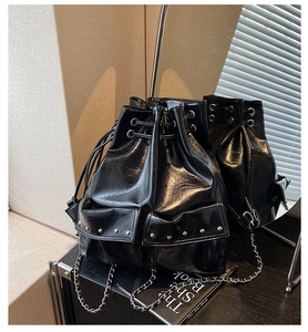 Detail of black glossy bucket bag with silver studs and chain straps in a modern setting