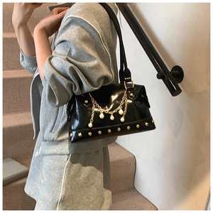 Detail of black patent leather shoulder bag featuring gold studs and pearl chain charms