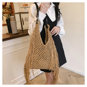 Detail of woven tote bag with long bohemian fringes and black leather handle detail