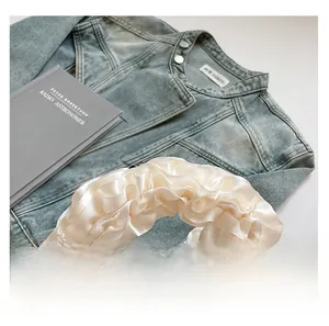 Close-up of ruffled satin handle on white lace handbag over denim jacket and book