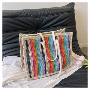 Close-up of rainbow striped woven tote bag with white leather handles on a white fabric