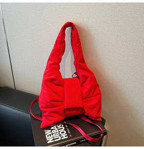 Detail of red bow-shaped quilted nylon tote bag with puffy padded texture and strap