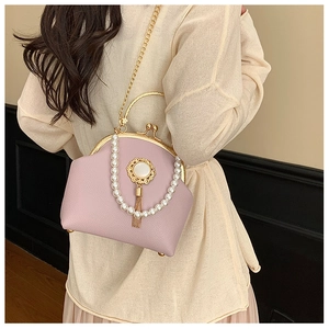 Detailed view of pink pebble leather clutch with pearl chain, gold fringe, and metal handle