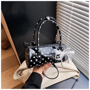 Close-up of a cylinder handbag with white polka dots and delicate pearl bow charm