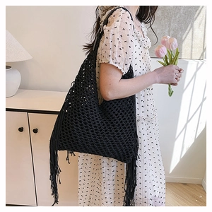 Detail view of black crochet knit tote bag featuring long decorative tassels and woven texture
