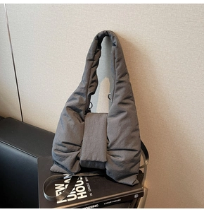 Detail of dark grey quilted puffer tote bag with bow decoration on a black book