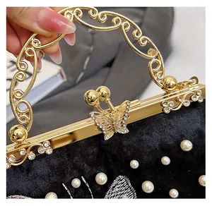 Détail d'un sac de soirée en velours avec poignée dorée et fermoir papillon diamants