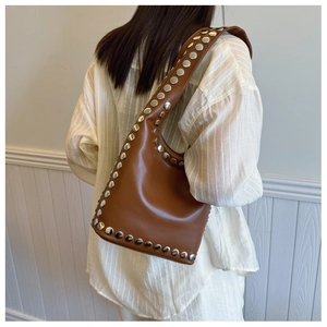 Detail der braunen Leder-Beuteltasche mit silbernen Nieten und breitem Schultergurt-Design