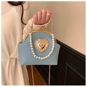 Detail of blue leather bag with gold heart relief, pearl handle, and metal chain