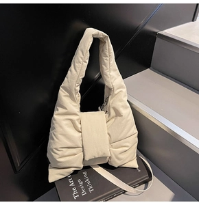 Detail of cream quilted tote bag featuring a large bow flap and adjustable strap