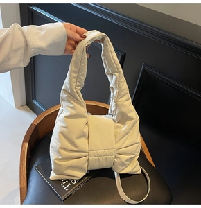 Detail view of cream quilted bow tote bag with soft padded texture on a black chair