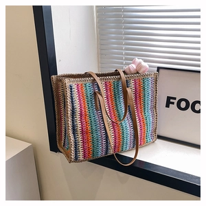 Close-up of rainbow striped straw tote bag with brown PU leather handles on windowsill