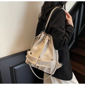 Detail of cream hobo bag showing glossy texture, drawstring, silver rivets and chain straps