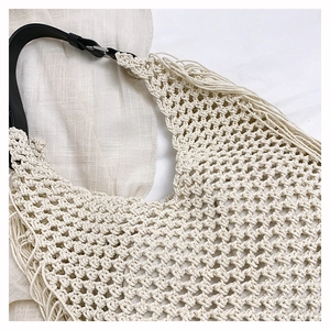 Close-up of bohemian knit bag featuring woven cream mesh, fringe detail, and black leather strap