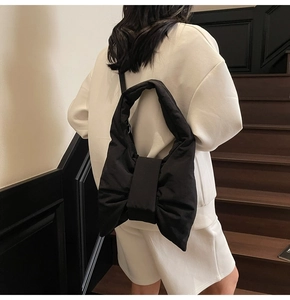 Detailed view of black nylon tote bag with bow design worn on shoulder by a model