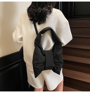 Detailed view of large black bow-shaped padded tote bag worn by a model in white