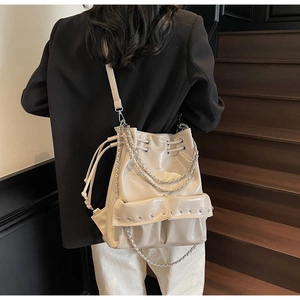 Detail view of beige bucket bag with metal chain straps and front rivet pockets