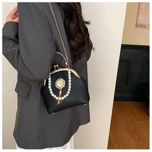 Detail of black pebbled leather bag with gold kiss lock, pearls, and metallic chain strap