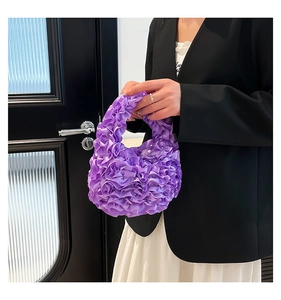 Detail of purple ruched evening handbag with pleated satin texture held by a model