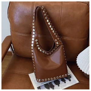 Detailaufnahme der braunen Ledertasche mit Silbernieten auf einem Vintage-Sofa