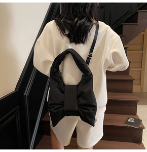Detail of oversized black bow-shaped tote bag worn by a model in a minimalist setting