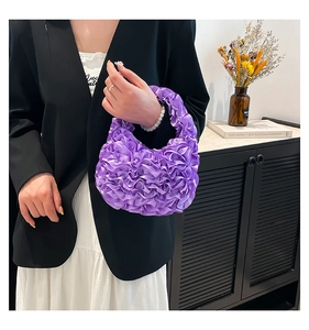 Detail of purple pleated silk handbag with ruffled texture held by model in casual setting