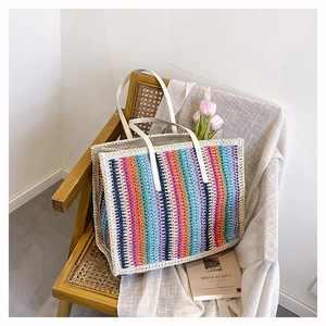 Close-up of rainbow striped straw tote bag with white faux leather handles on a rattan chair