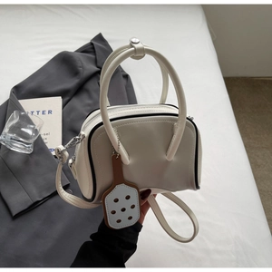 Detail of cream bowling bag with PU leather texture, dual handles and charm decoration