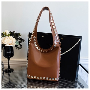 Detail einer braunen Leder-Hobo-Tasche mit silbernen Metallnieten und breitem Schultergurt