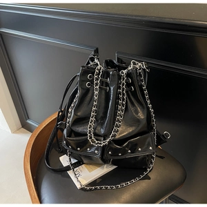 Detail of high-gloss black bucket bag featuring silver rivet studs and chain strap