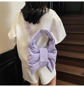 Detail of light purple puffy bow tote bag worn by a model against a minimalist wall