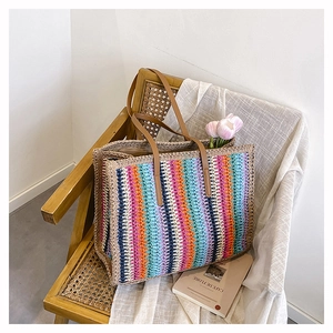 Detailed close-up of rainbow woven straw tote bag with brown leather handles on a chair