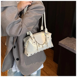 Detail of a creamy white studded tote bag with pearl chain shown on a grey suit outfit
