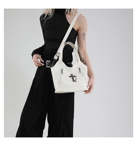 Detail of white gothic tote bag featuring black cross pendant and metal chain accents